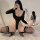 Woman wearing black long-sleeve bodysuit with thigh-high stockings, posing on white rug — sensual ice silk bodysuit for women...
