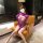 Woman wearing purple sheer mesh bodysuit with long sleeves, seated on leather chair in modern room.