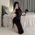 Woman in black sheer bodycon dress with high slit, holding a rose, posing on bed – perfect for nightclub or party.