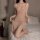 Woman kneeling on bed wearing sheer pink mesh slip dress with high split, part of sexy mesh slip dress lingerie set.