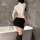 Woman wearing yeyu white long-sleeve crop top and black bodycon mini skirt, posing by bathtub in elegant lingerie set.