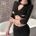 Woman wearing black yeyu long-sleeve bodycon lingerie set with cutout top and mini skirt, posing beside a white bathtub.