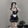 A woman poses in a black maid costume featuring lace apron, ties, and ruffled details, capturing her reflection on a smartpho...