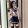 A woman poses in a mirror wearing a sailor-style bikini top with a bow tie and pleated skirt, paired with patterned stockings...