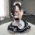 A woman wearing a black and white maid cosplay dress with ruffles, bows, and a cat paw design, sitting on a fluffy rug indoor...