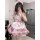 A woman wearing a cute maid costume cosplay outfit, featuring a soft pink lolita-style dress with ruffles, bows, and cat ears...