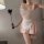 Woman wearing pink maid costume lingerie set with lace trim, sheer bodice, ruffled apron, and matching garter holding a feath...