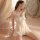 Woman wearing sheer lace nightwear with tie-front design, sitting on bed surrounded by soft curtains.
