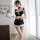 Woman modeling black lace maid bodysuit with white trim, backless cutout, and bow details in bright room.