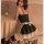 Woman in black maid costume with lace trim and white bow, posing beside a table with candles.