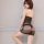 Woman wearing black sheer mesh bodysuit with lace thong and skirt, posing seductively against white wall.