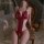 Woman wearing mannyan red lace open-crotch bodysuit with sheer mesh, posing on ornate chair in romantic bedroom setting.