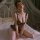 Woman wearing mannyan sensual lace bodysuit, sheer mesh with polka dots and pearl beading, posing on bed in romantic setting.