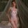 Woman wearing mannyan white lace bodysuit with bow detail and garters, posing on a bed with sheer canopy.