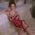 Woman in mannyan red lace bodysuit with bows, sheer open-crotch design, posing on white bed—sensual nightwear.