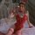 Woman wearing mannyan red lace bunny costume with floral trim, adjustable straps, and fishnet stockings on a bed.