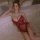 Woman modeling mannyan red lace bodysuit with beaded straps, polka dot mesh, and ruffled trim on bed.