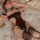 Woman wearing mannye qing red and black lace bodysuit with underwire, lying on bed with sheer fabric.