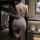 A woman stands facing away from the camera, wearing a sheer black dress with a plunging neckline and a fitted silhouette. she...