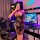 A person poses in a gaming room wearing a black lace dress with sheer details, featuring a vintage chinese-style design and t...