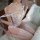 Woman wearing white sheer mesh bodysuit with spiderweb lace cutouts and open-crotch design, sitting on bed.