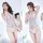 Woman modeling white lace mesh bodysuit with open-crotch design, sheer fabric, and delicate straps in bright bedroom setting.