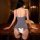 Woman wearing black open-crotch bodysuit lingerie set, back view on wooden table in dimly lit room.
