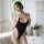 Woman wearing black sheer striped bodysuit lingerie in bright bedroom setting.