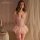 Woman modeling pink manyan lace bodysuit with corset waist trainer and sheer sleep dress in romantic bedroom setting.