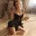 Woman wearing black manyan sheer lace sleep dress with adjustable straps, open front design for small bust, sitting on bed.