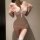 Woman wearing pink sheer lace lingerie set with floral pattern and white stockings, posing seductively indoors.
