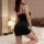 A woman poses on a bed wearing a black midnight allure deep v-neck slip dress, featuring a seductive wine red satin finish, h...
