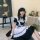 A woman wearing a black and white lolita maid dress with ruffles, sitting indoors next to an easel painting. the outfit featu...