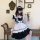 A person wearing a black and white lolita maid dress with ruffles, sitting on a bench holding flowers, styled for cosplay and...