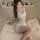 Woman wearing moonlit memory lace mesh slip dress, sitting on cream tufted bed with photos pinned behind her.