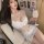 Woman in white lace mesh sleepwear set with adjustable straps, holding a fluffy drink, seated on a cozy chair.