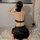 A woman sits on a rug wearing a black night charm original chinese-style lace cheongsam lingerie set with chains and sheer hi...