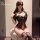 Woman wearing black vinyl bodysuit with lace detailing and thigh-high stockings, seated on a stool.