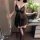Woman wearing black lace sheer sleep dress with open-crotch design, holding wine glass in elegant bedroom setting.