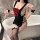 A woman poses elegantly in a black maid costume with lace details and a red bow, holding a glass of champagne beside a bathtu...
