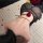 Woman in black sheer mesh backless nightgown with rose on spine, lying on white rug with rose petals.