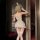 Woman wearing night-silk bunny girl lingerie set with bunny ears, sheer stockings, and ruffled skirt in a dimly lit room.
