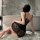 Woman in black lace slip dress with adjustable straps, sitting on fur rug beside bathtub, showcasing elegant back design.