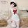 A woman poses wearing a white maid apron set with red bows, lace details, and stockings, styled for a feminine look.