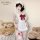 A woman wears a white maid apron set with red bows, lace details, and stockings, posing next to teddy bears. the outfit featu...