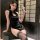 A woman poses elegantly in a black sheer cheongsam-style lingerie set, featuring cut-out details and lace stockings, exuding ...