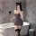 Woman in gray lace-back sleepwear set with cat ears, holding feather wand, posing by bathtub for romantic night.