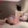 Woman in pink sheer lace mesh sleep dress with strappy back, sitting on bed with rose petals.