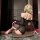Woman wearing black mesh nightse erotic lingerie set with bondage straps, posing on floor in dimly lit room.