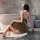 Woman in shiny gold nightse lace slip dress, seated by bathtub, back view, elegant clubwear bodysuit for small bust.